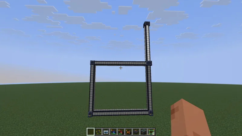 A square gate standing on grass with a tall pole rising from its upper right corner